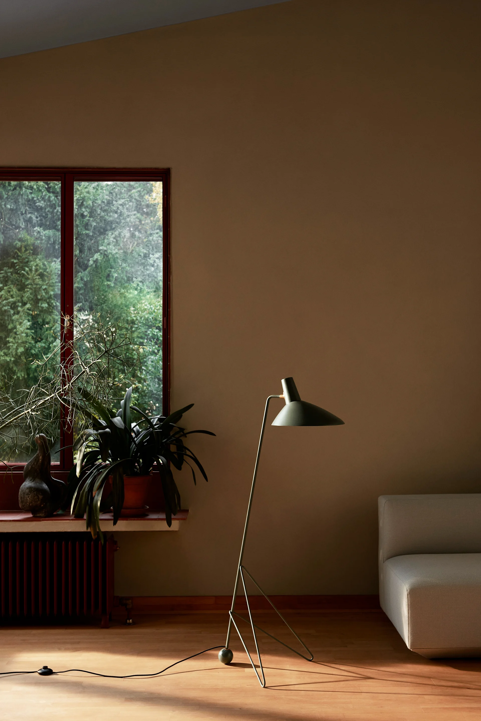 Bild som visar Tripod golvlampa  från danska &Tradition i en mörk mossgrön färg ståendes på trägolv i vardagrsum.