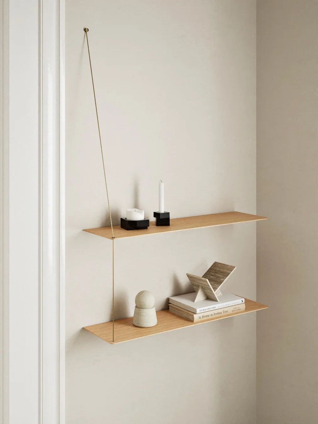 Två minimalistiska hyllor i ljust trä, upphängda med en smal mässingsstång. Övre hyllan har två vita ljus. Nedre hyllan har böcker och inredning.