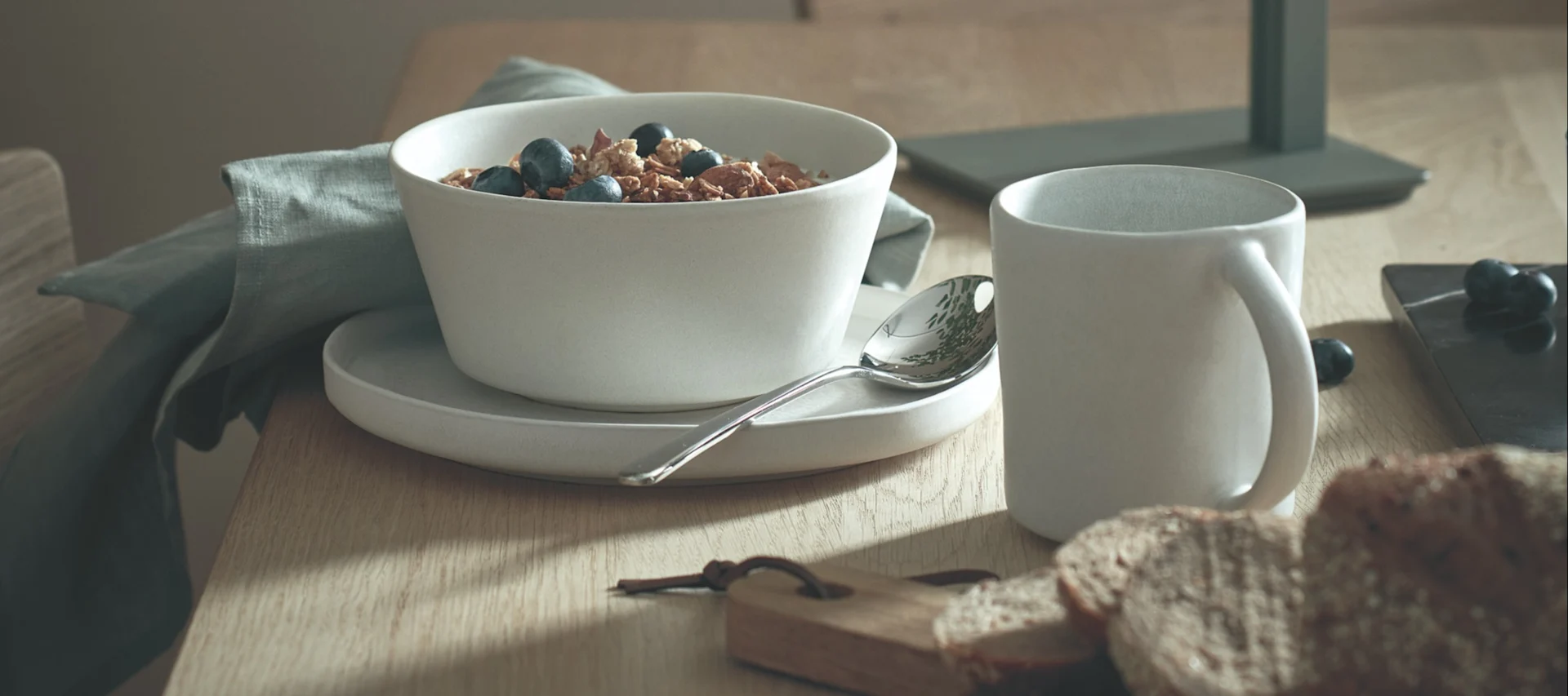 Matplats-inspiration i form av dukning med vitt Sandsbro-porslin från Scandi Living tillsammans med grön linneservett, placerat på såpat ekbord c18 från Fredericia Furniture.