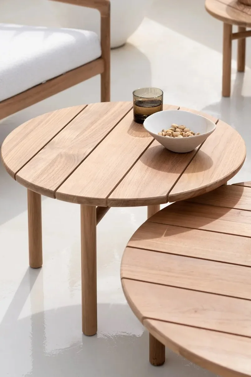 Bild som visar Quatro loungebord i obehandlad teak från Ethnicraft. Bordet är runt med breda blankor och ett underrede med fyra smala ben.