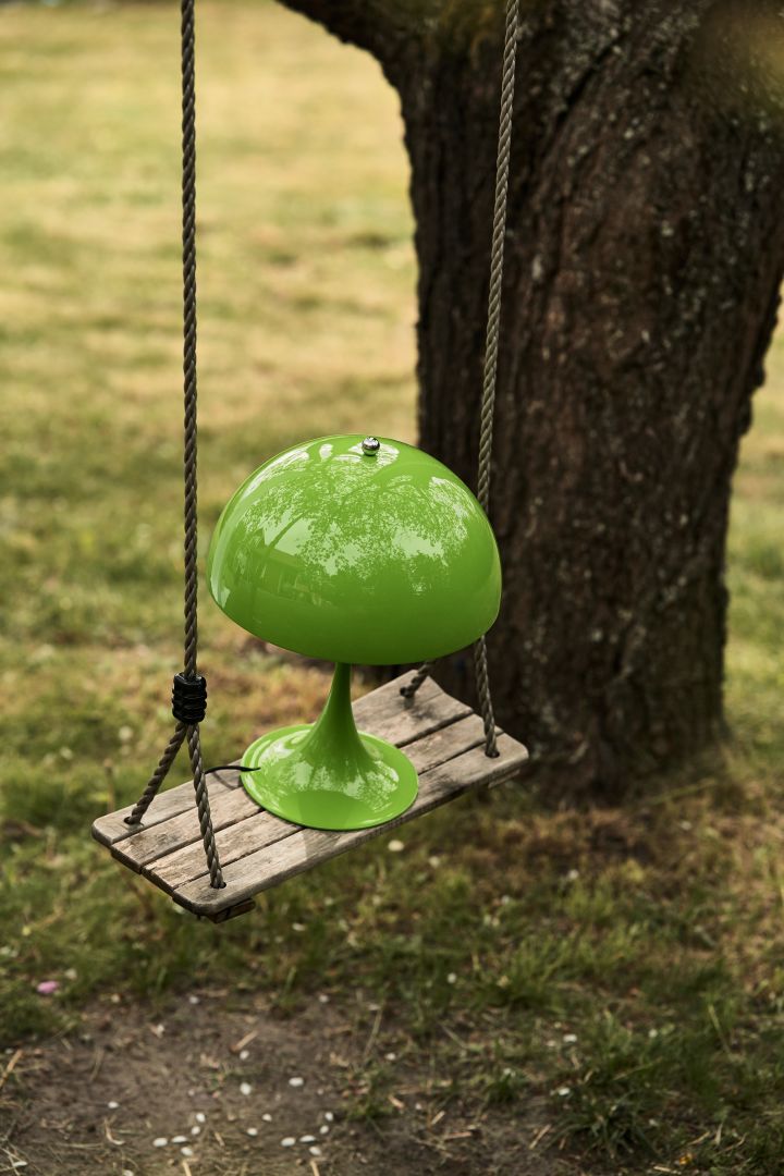 Bild som visar Panthella portabel lampa i grön från Louis Poulsen, här placerad på en gunga utomhus.