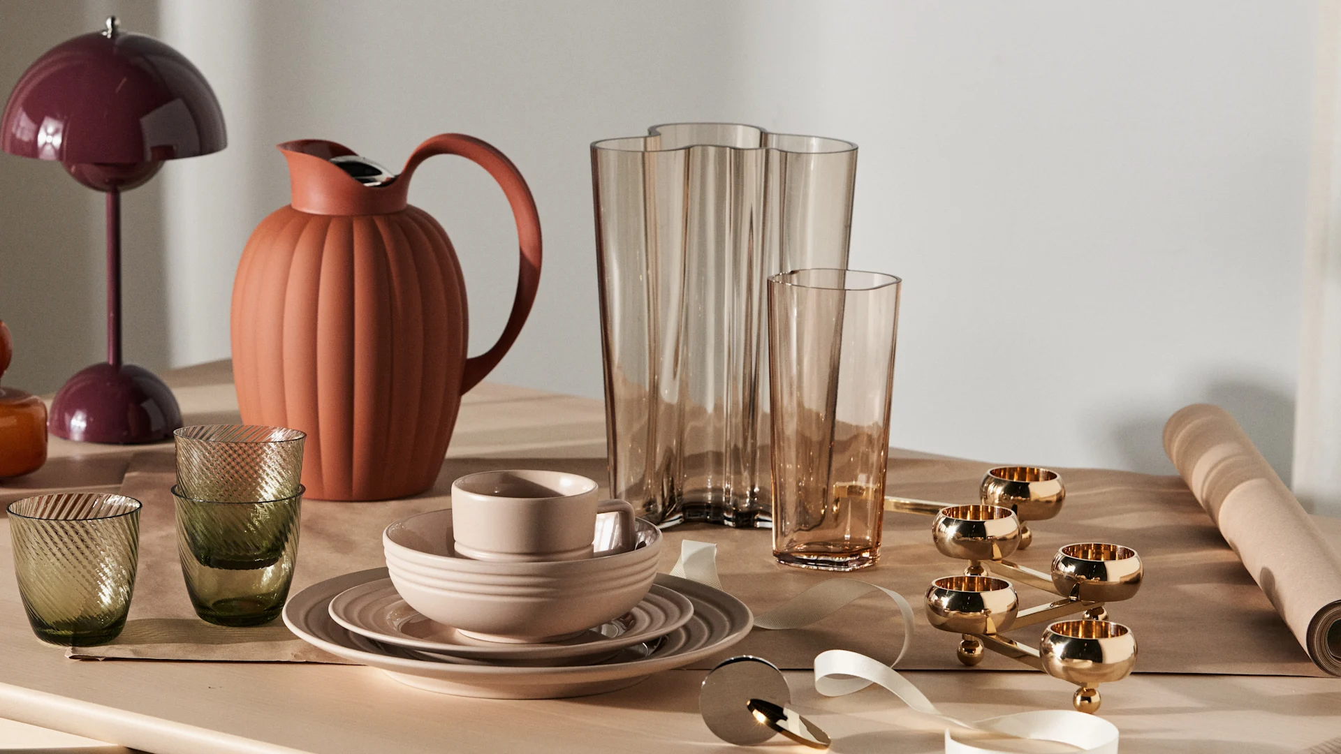 Presenttips till den designintresserade och tips på klassiska examenspresenter uppdukade på ljust träbord. Här står Flowerpot portabel lampa i färgen dark plum tillsammans med Bernadotte termoskanna i terracotta, Alvar Aalto vas i rio brun och Lines porslin i beige från NJRD.