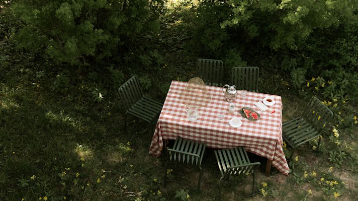 Bild som visar Pallisade utemöbler i form av bord och stolar i grönt från varumärket HAY. Här med en vacker röd- och vitrutig duk på.
