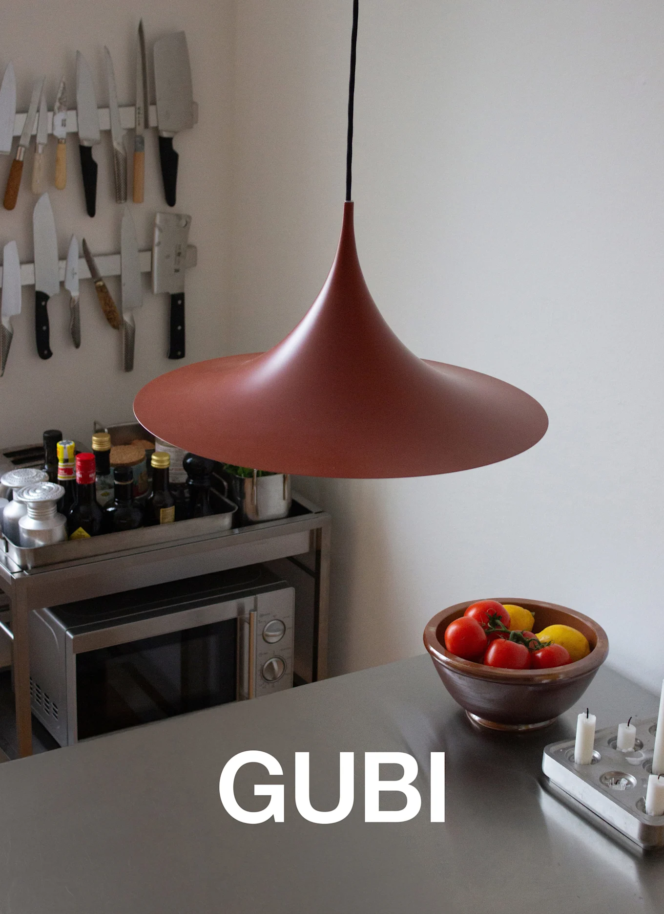 Ett oregelbundet svart soffbord med smala ben på en lila matta, med en bok och glaskopp, vid en vit öppen spis.