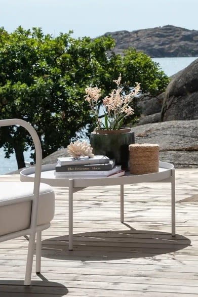 Bild som föreställer Saltö loungebord från Skargaarden. Ett runt bord tillverkat i pulverlackerat aluminium, här placerat på uteplats med trätrall bredvid Bönan loungesoffa i vitt.