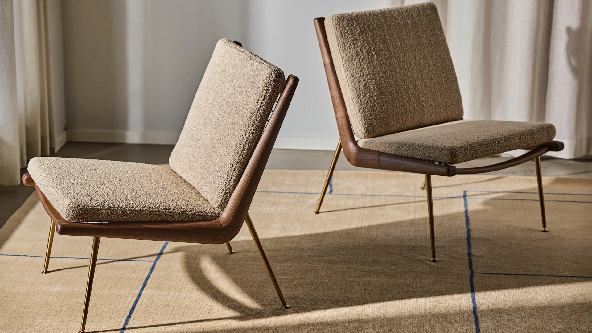 Bild som visar två Boomerang-fåtöljer av designduon Hvidt & Mølgaard, här i beige med valnötsben stående på Cruise AP12 matta i beige med linjerat mönster i blått.