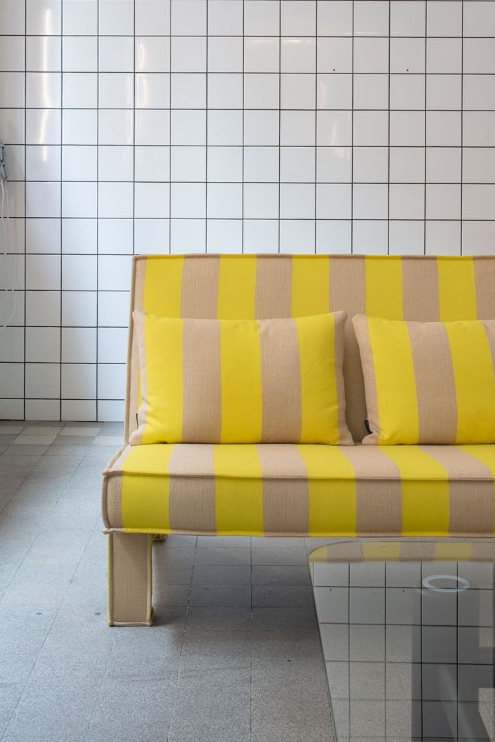 Bam soffa i gult från svenska Massproductions placerad mot helkaklad vägg