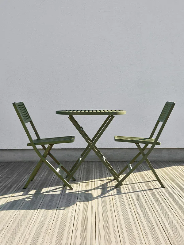 Två gröna hopfällbara stolar och ett matchande bord på ett randigt trädäck mot en vit vägg.