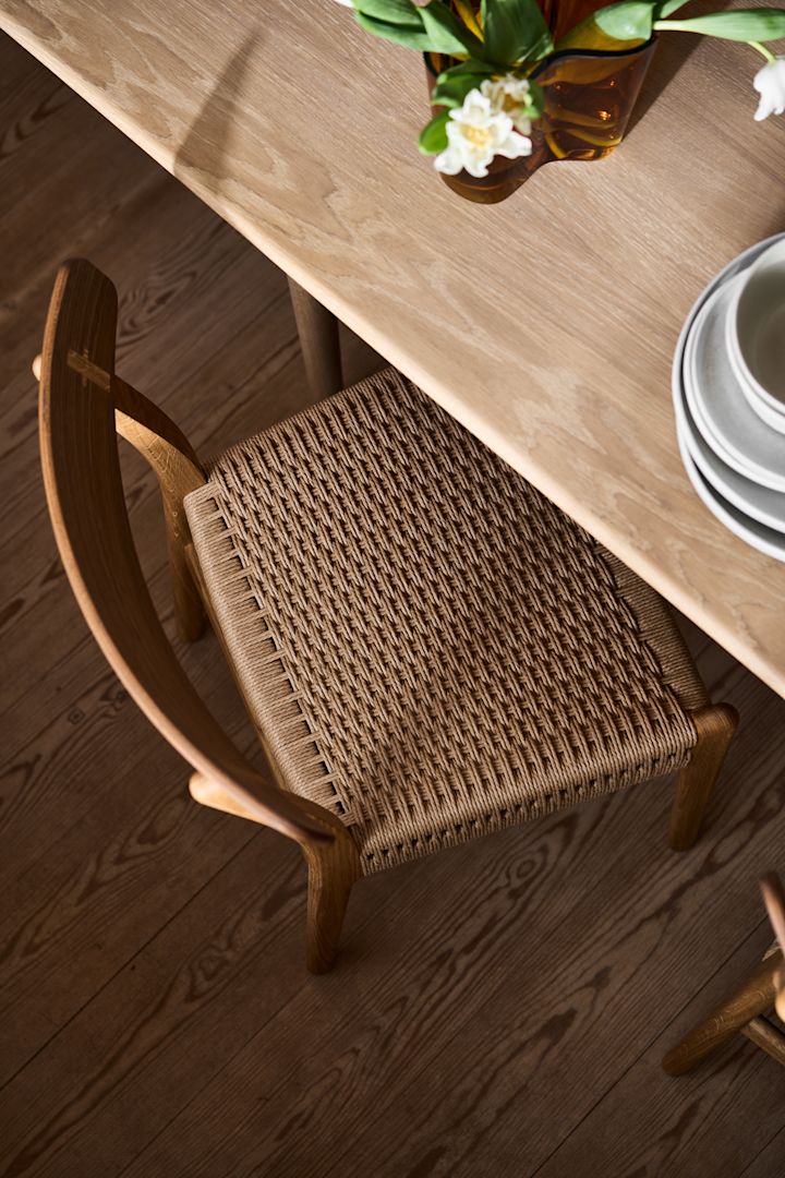 Hur inreder man med klassiska möbler och designklassiker, här närbild ovanifrån på CH23 stol från Carl Hansen & Son vid matbord i ek, på bordet en Alvar Aalto vas i bärnsten med vita tulpaner i.