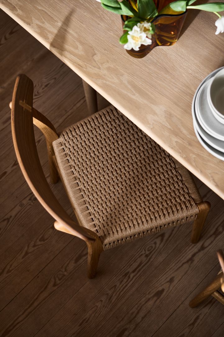 Hur inreder man med klassiska möbler och designklassiker, här närbild ovanifrån på CH23 stol från Carl Hansen & Son vid matbord i ek, på bordet en Alvar Aalto vas i bärnsten med vita tulpaner i.