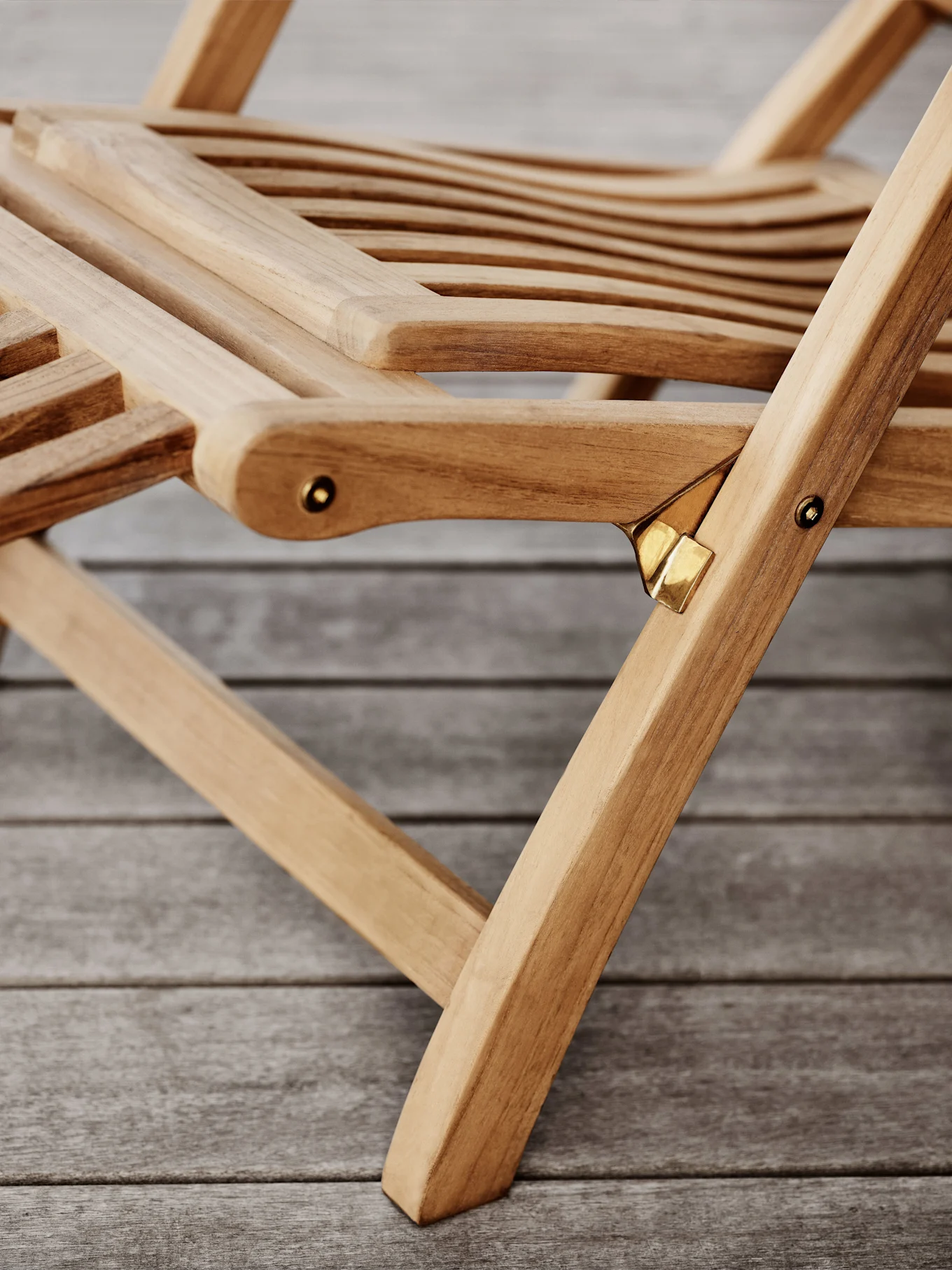 Närbild av en hopfällbar trästol med ribbor och mässingsdetaljer på ett trägolv.