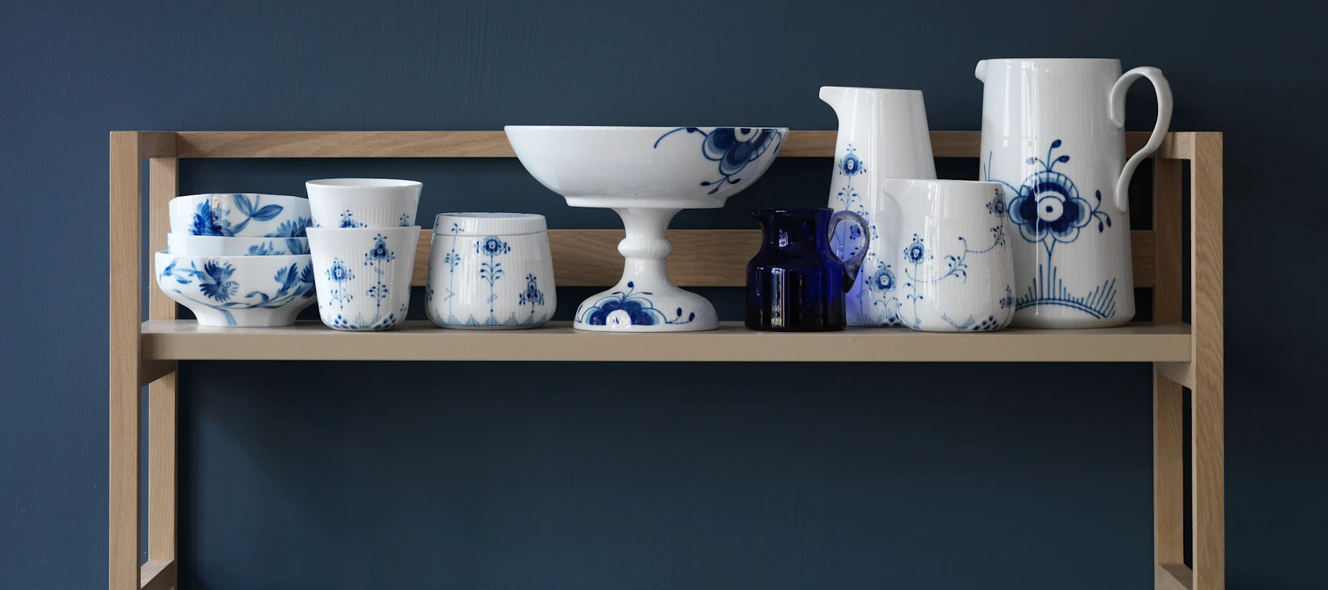 Blåvitt porslin från Royal Copenhagen, Blue Elements-porslin på trähylla mot blå vägg.