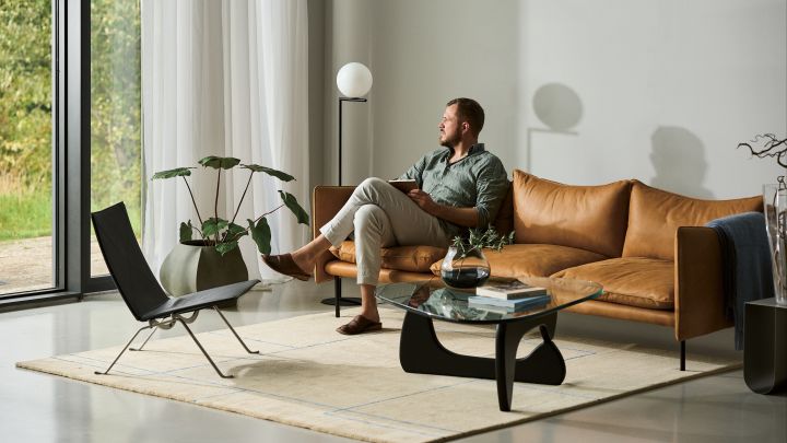 Ett tips bland snygga golvlampor är IC Lights F1 från Flos, här placerad i vardagsrum bredvid cognacsbrun lädersoffa med beige matta och soffbord med glasskiva.