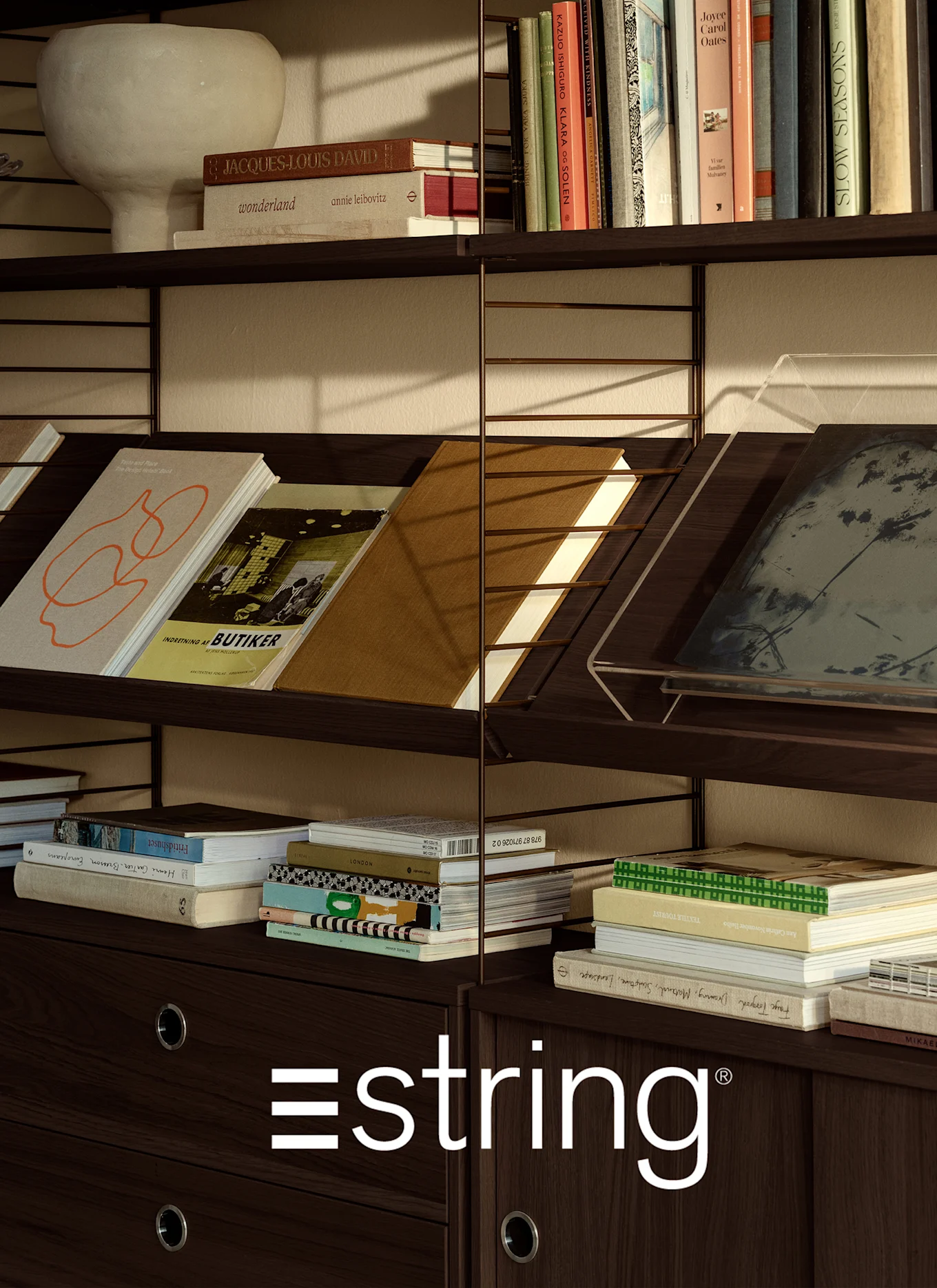 Mörkbrun trähylla med diverse böcker, en ljus vas och den vita 'estring'-logotypen längst ner.