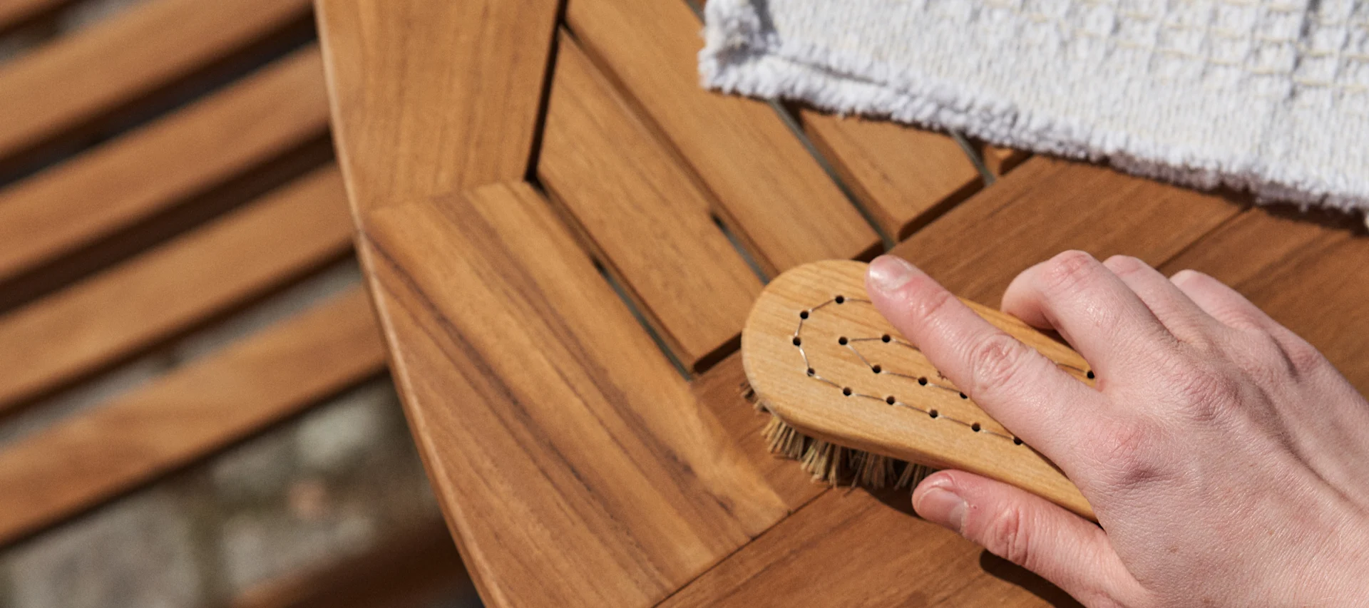 Skötselråd och tips på hur du tar hand om dina utemöbler på bästa sätt, här skrubbas ett utebord i teak med rengöringsborste och torkas med mjuk trasa.