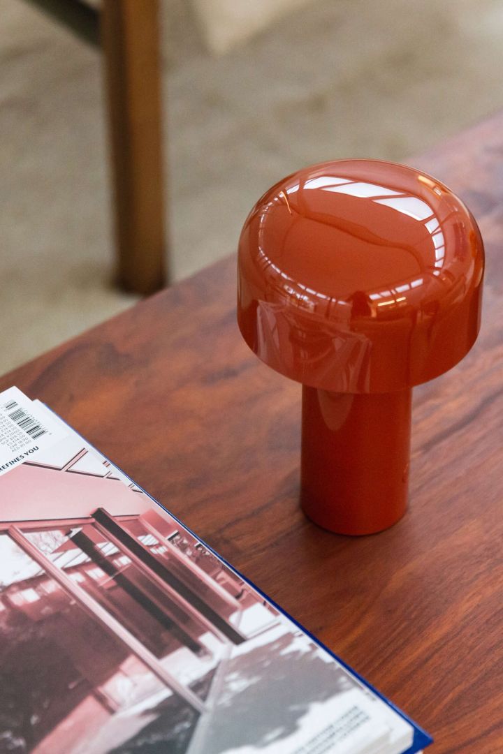 Bellhop portabel bordslampa i orange från Flos, en av flera populära lampor i höst, här placerad på ett mörkt träbord.