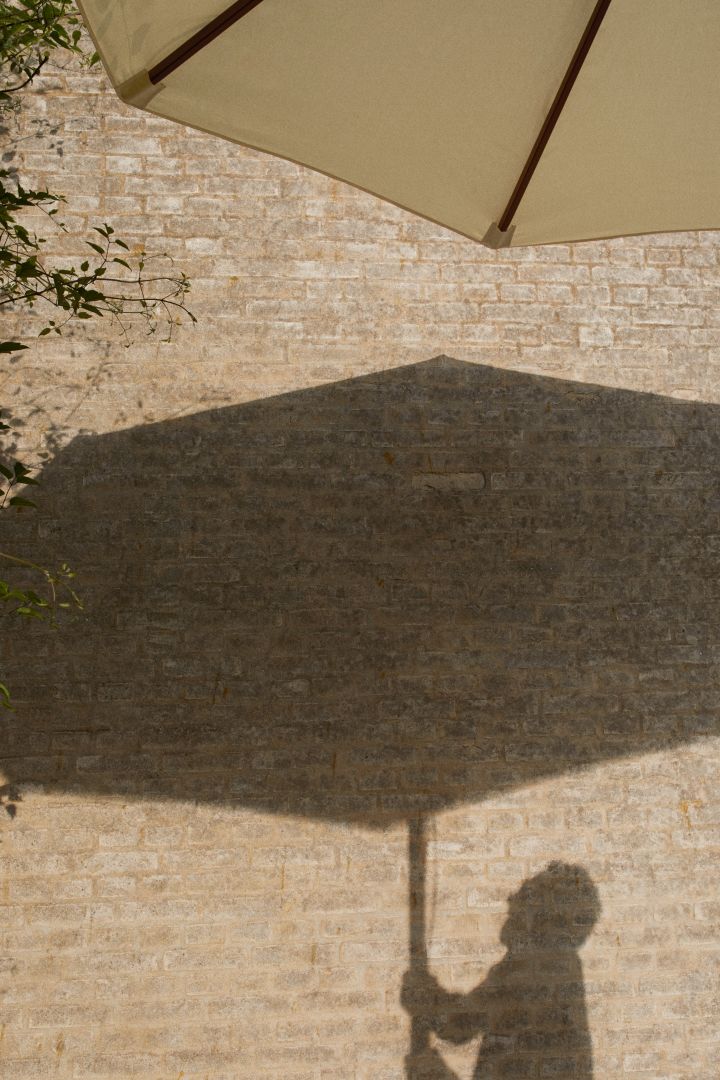 Messina parasoll i vitt från varumärket Skagerak med skuggaavbildning mot tegelvägg.