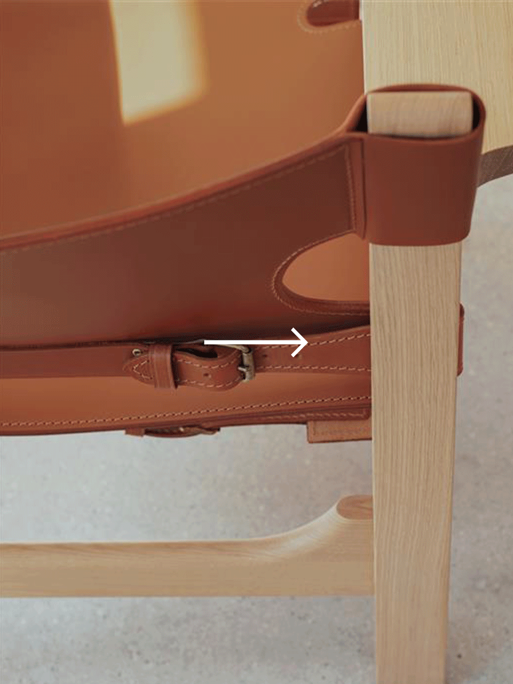 Närbild av en grå, rund sits på en trästol, med vit pil som pekar horisontellt.