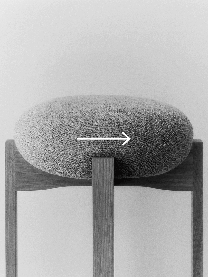 Närbild av en grå, rund sits på en trästol, med vit pil som pekar horisontellt.