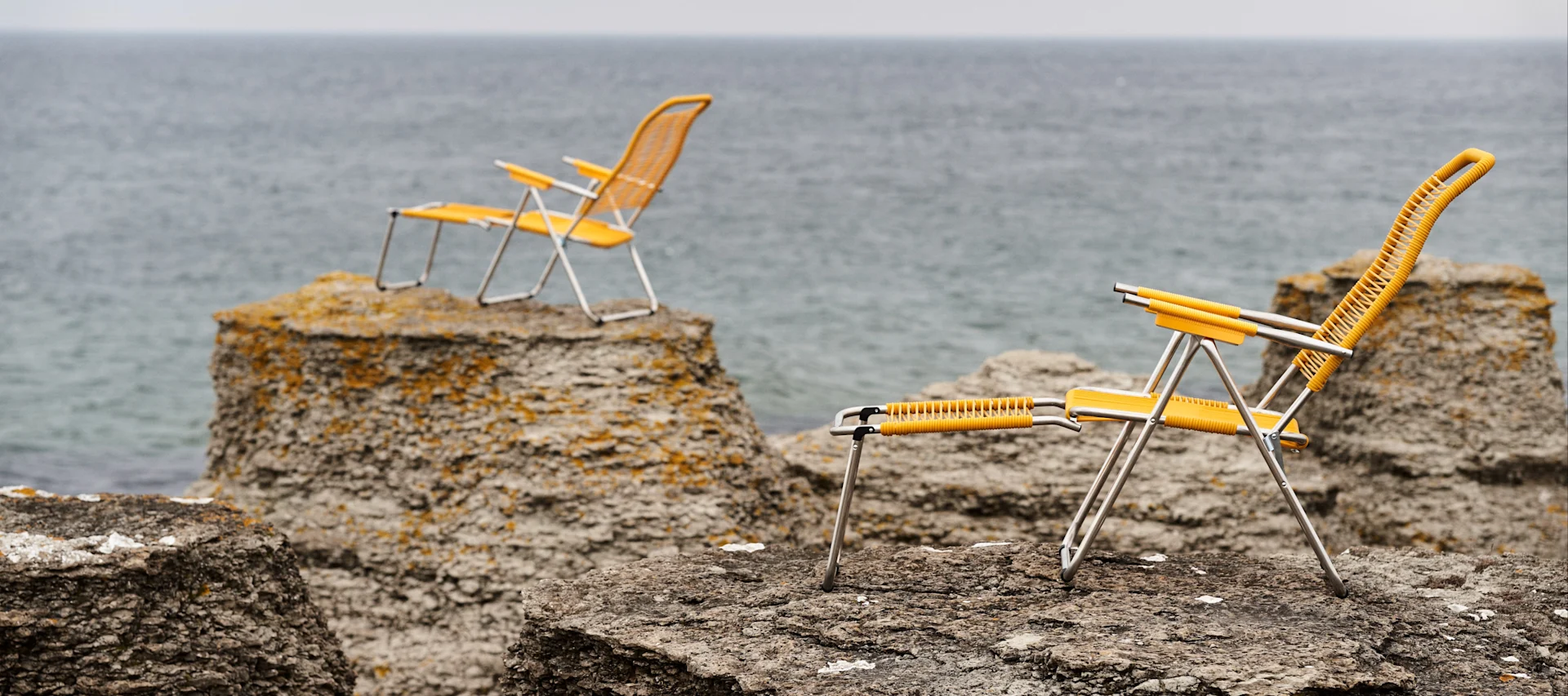 Snygga solstolar & sköna solsängar - bild som visar en gul Spaghettil solstol från Fiam, placerad på raukar med havet framför.