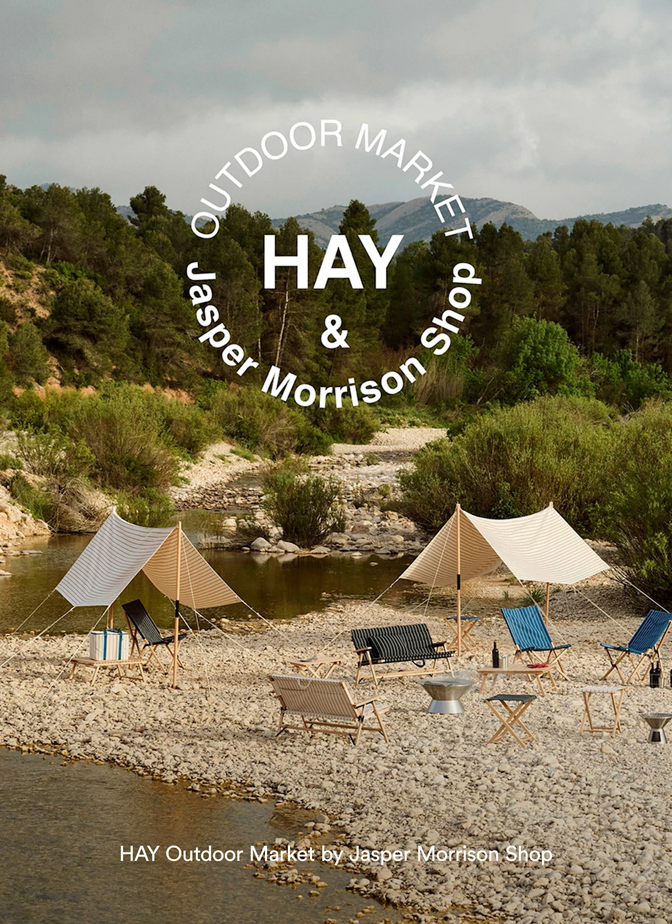 Utomhusmarknad på stenstrand med randiga markiser, hopfällbara stolar och bord vid en flod. Text: HAY Outdoor Market by Jasper Morrison Shop.