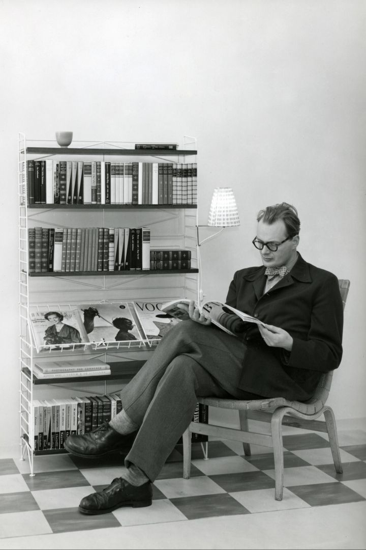Bild som visar Nisse Strinning sittandes med en tidning framför en Stringhylla.