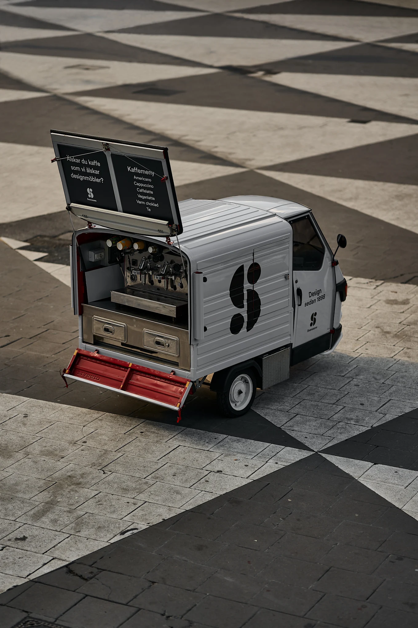 Bild som visar en tuktuk-bil på Sergels Torg i Stockholm. Tuktuken är vit med Svenssons logotyp i svart på sidan.